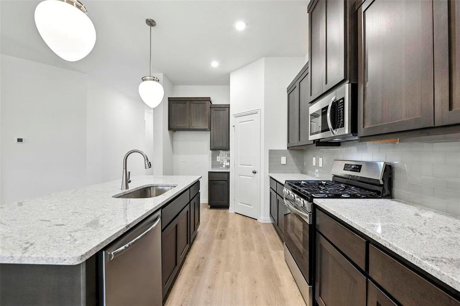 Kitchen featuring appliances with stainless steel finishes, light wood-style flooring, backsplash, dark brown cabinetry, and light stone counters