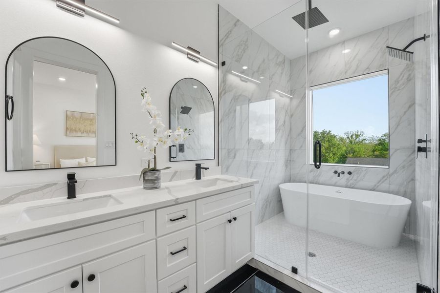 Luxurious primary bathroom featuring a double-sink vanity with quartz countertops, dual arched mirrors, marble-look tile, a glass-enclosed walk-in shower, and a freestanding soaking tub flooded with natural light from a large picture window.