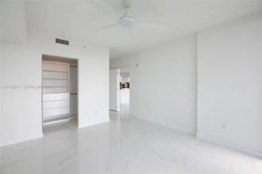 Interior space featuring white stone-finish tile flooring, ceiling fan with integrated lighting, and walk-in closet with built-in shelving and drawer units