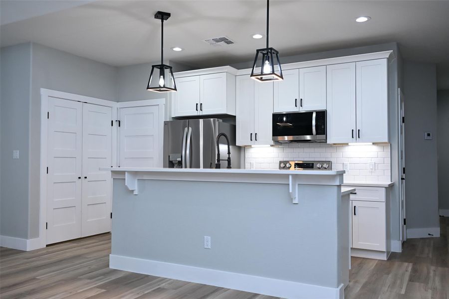Kitchen with white cabinets, stainless steel appliances, backsplash, dark wood-type flooring, and a kitchen bar