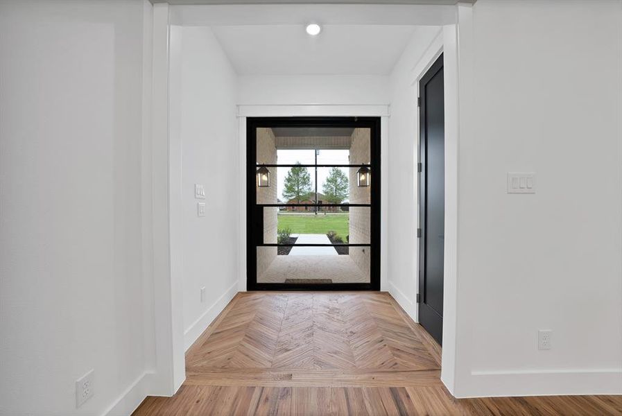 Entrance featuring a dark framed glass door, herringbone pattern wood flooring, and a dark interior door