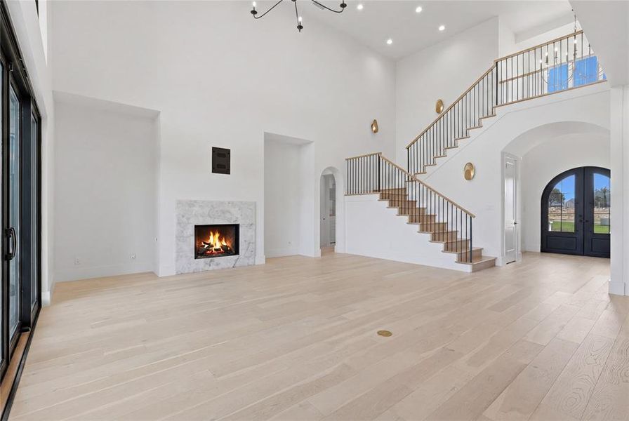 Grand entry and living space featuring high ceilings, light wood-finish flooring, a contemporary fireplace with a stone surround, and a sweeping staircase with a black iron railing and wood handrail