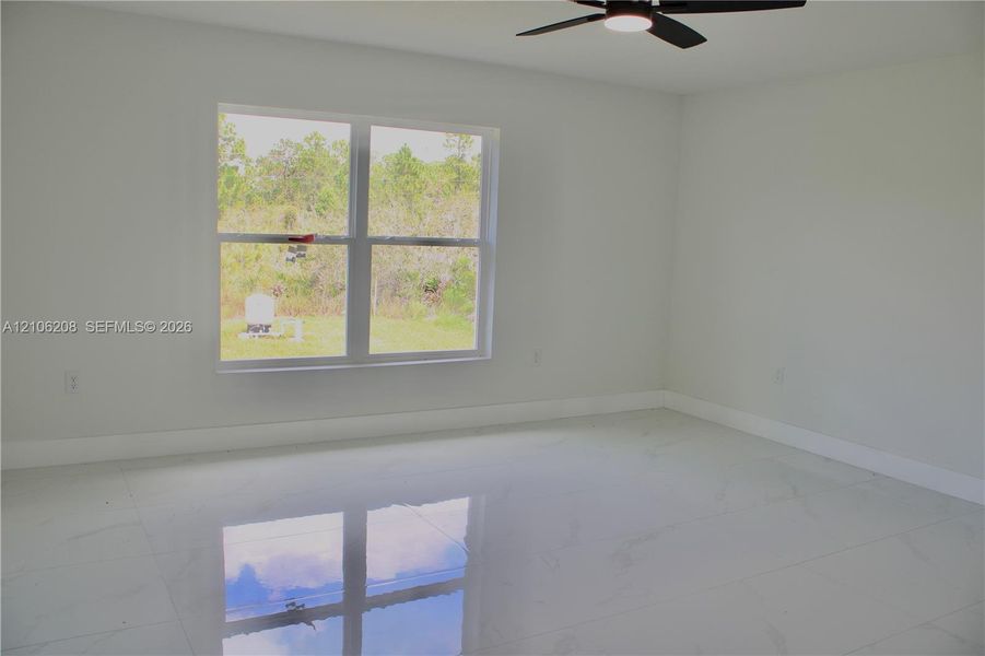 Spacious interior featuring large-format tile flooring, neutral wall tones, a ceiling fan with integrated lighting, and a multi-pane window