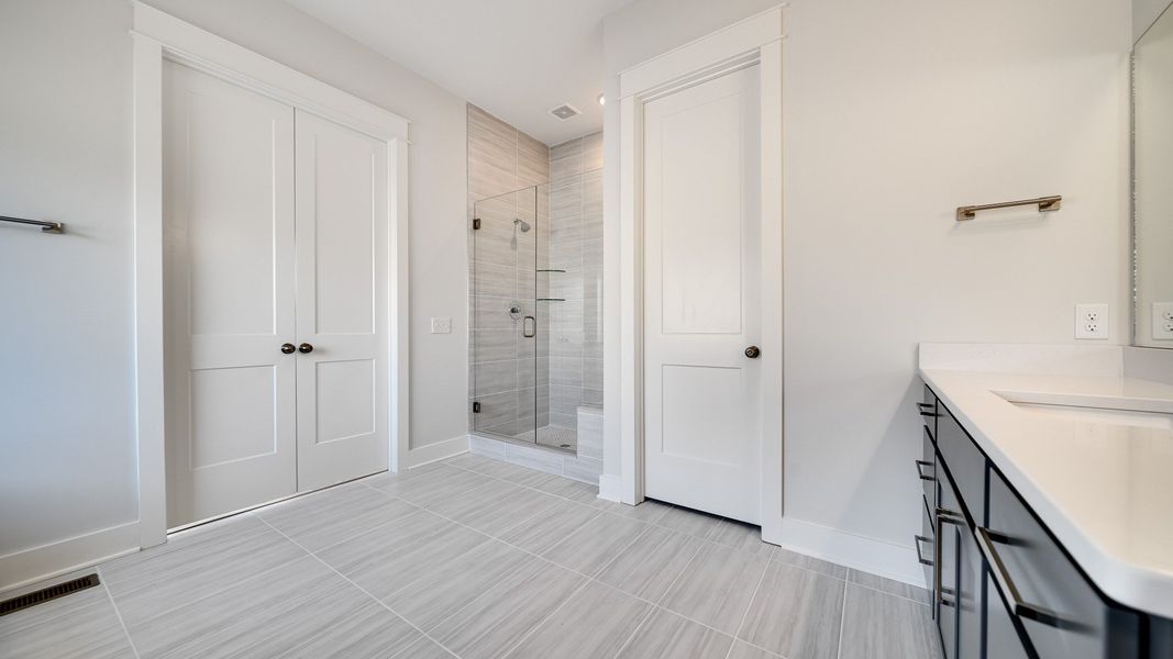 Large tiled bathroom with multiple vanities, glass shower enclosure, and freestanding tub