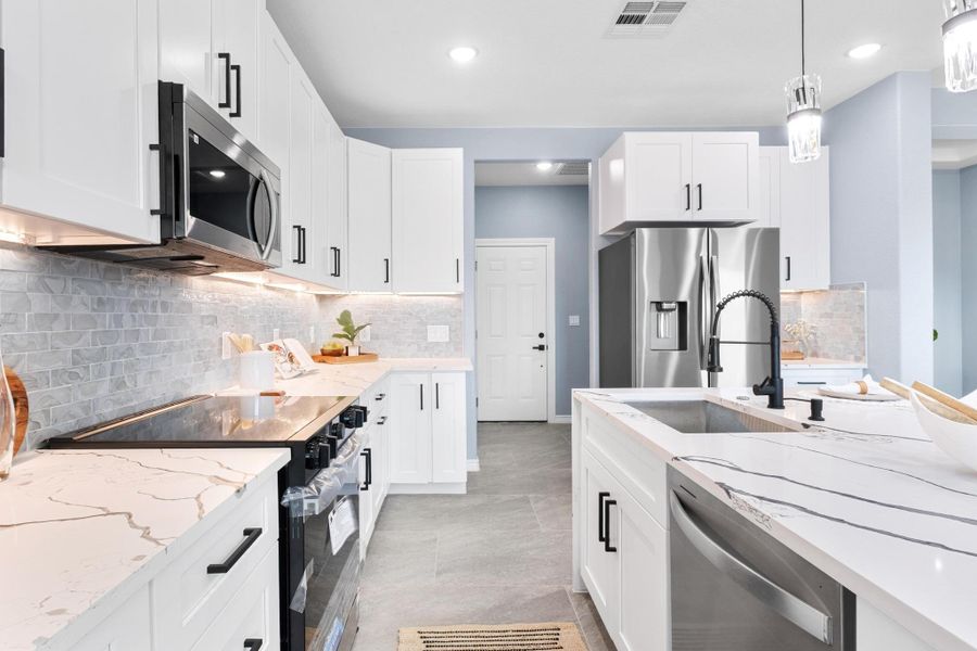 Kitchen with appliances with stainless steel finishes, decorative backsplash, light stone countertops, white cabinetry, and recessed lighting Kitchen with appliances with stainless steel finishes, decorative backsplash, light stone countertops, white cabinetry, and recessed lighting