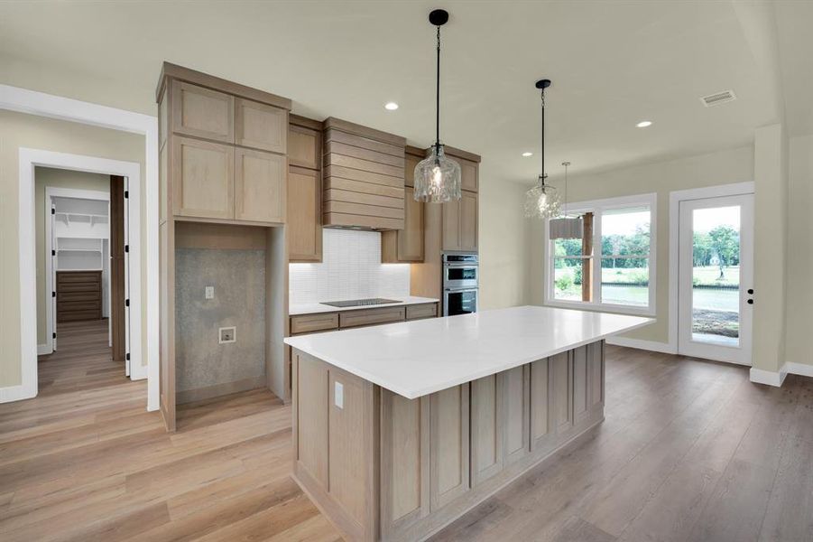 Kitchen with decorative backsplash, pendant lighting, a center island, light wood-type flooring, and premium range hood