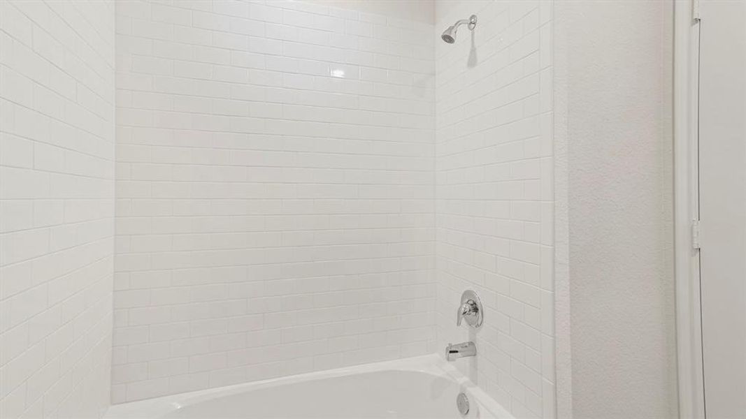 Bathtub-shower combination featuring white subway tile surround, polished chrome fixtures, and a white porcelain tub