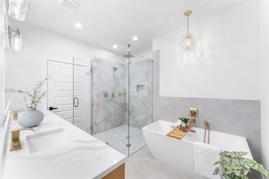 Bathroom with double vanity, a freestanding tub, a marble finish shower, and suspended lighting