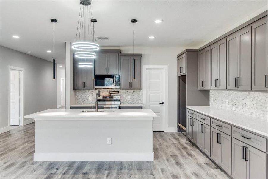 Kitchen featuring appliances with stainless steel finishes, decorative light fixtures, a kitchen island with sink, and light hardwood / wood-style floors