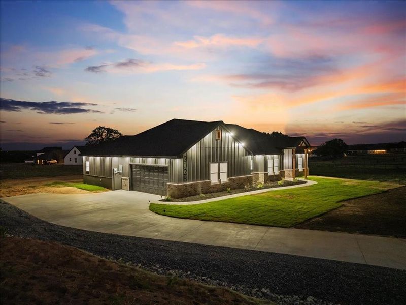 Modern farmhouse at dusk with siding, brick accents, bright exterior lighting, and great curb appeal.
