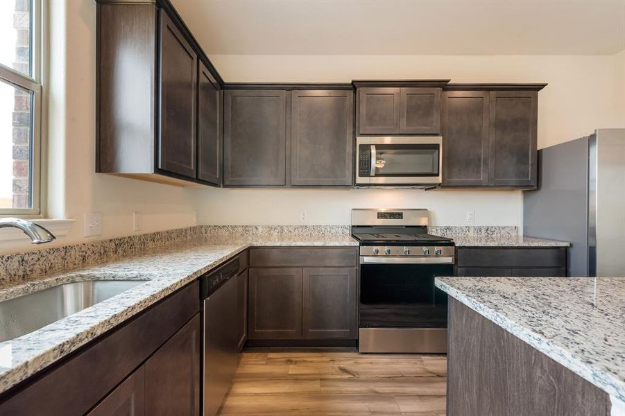 Kitchen featuring sink, light stone counters, dark brown cabinetry, light hardwood / wood-style floors, and appliances with stainless steel finishes