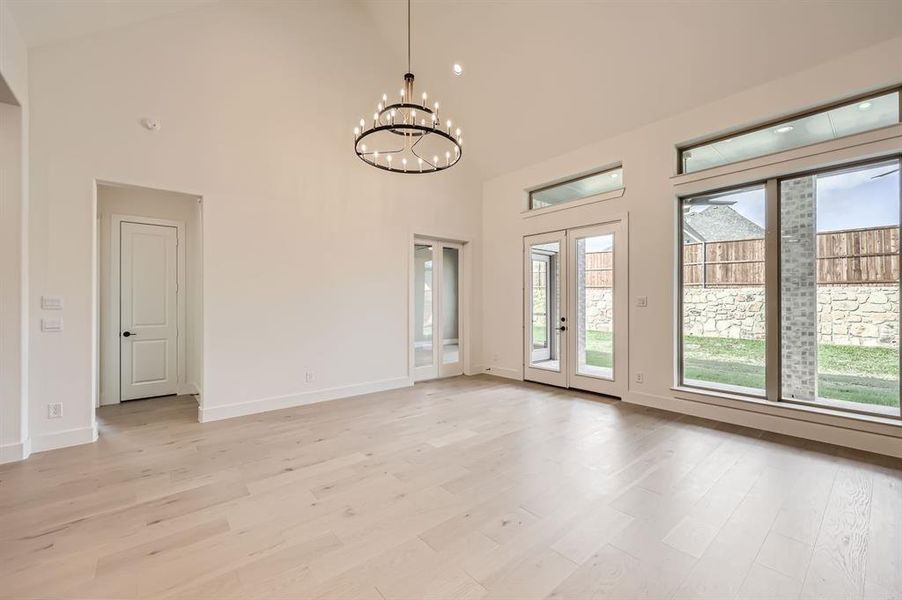 Empty room with high vaulted ceiling, light hardwood / wood-style flooring, and an inviting chandelier