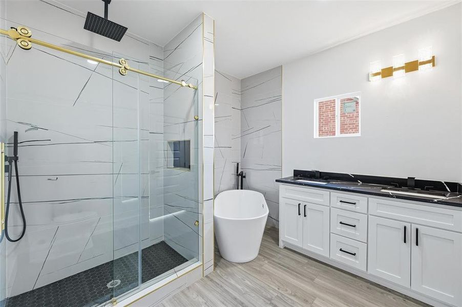 Full bathroom featuring double vanity, a stall shower, a freestanding tub, and light wood-type flooring Full bathroom featuring double vanity, a stall shower, a freestanding tub, and light wood-type flooring
