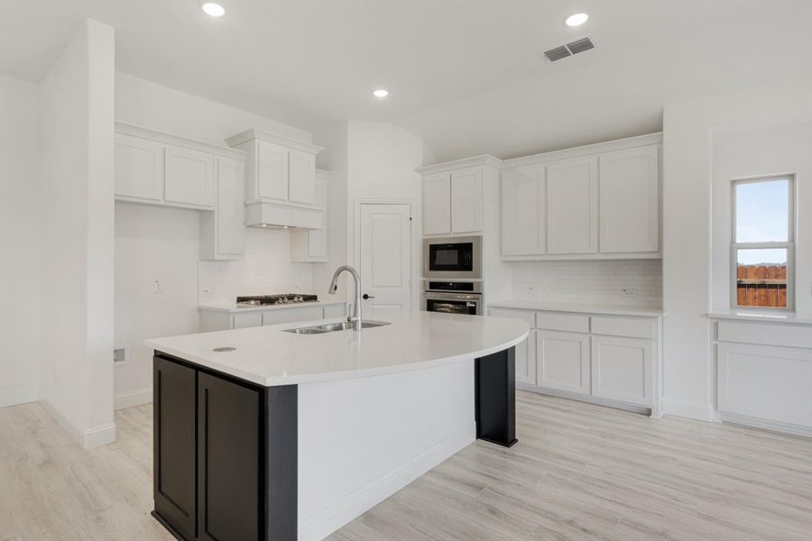 Kitchen with white cabinets, curved island with dark base, stainless steel appliances, and light wood floors
