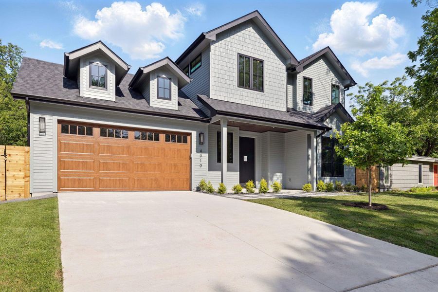 View of front of home with a shingled roof, driveway, a garage, and covered porch
