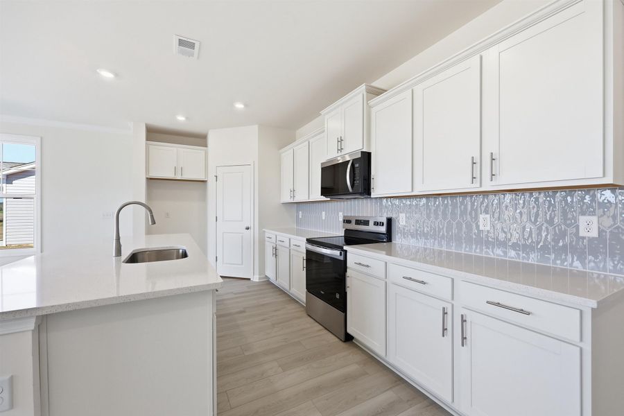 Kitchen with stainless steel appliances, light stone countertops, white cabinets, backsplash, and light wood-style floors