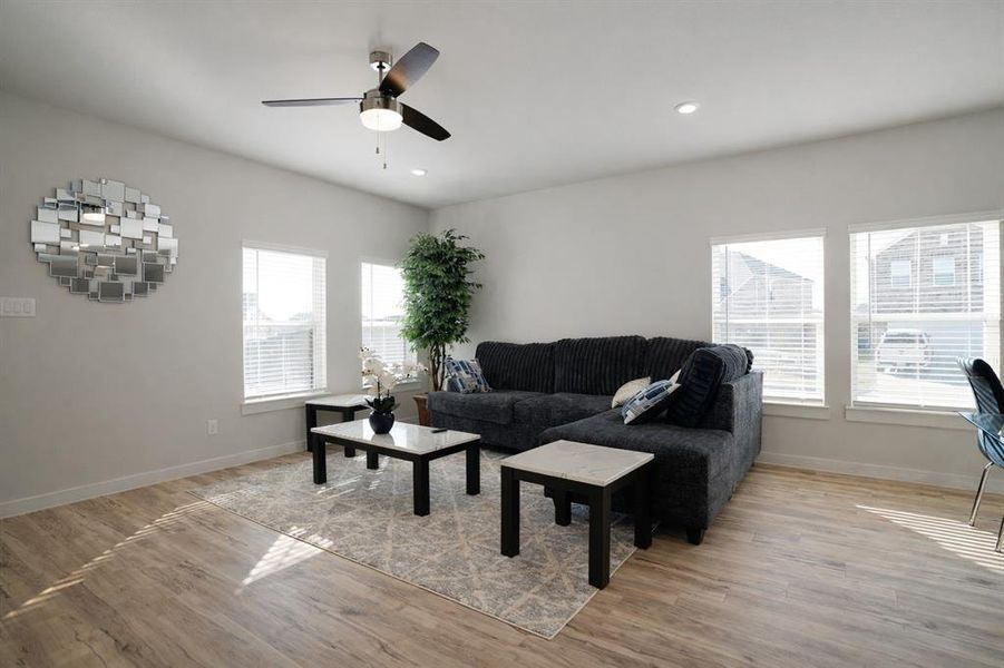 Spacious living area featuring wood-finish flooring, multiple windows with blinds, a ceiling fan with light fixture, and recessed lighting