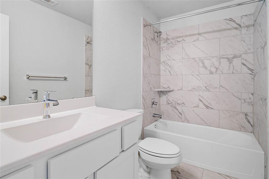 Secondary bath features tile flooring, bath/shower combo with tile surround, wood stained cabinets, beautiful light countertops, mirror, dark, sleek fixtures and modern finishes!