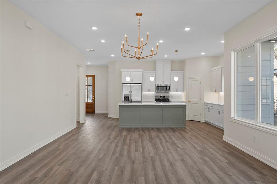 Kitchen featuring white cabinetry, a kitchen island, light countertops, hanging light fixtures, and appliances with stainless steel finishes Kitchen featuring white cabinetry, a kitchen island, light countertops, hanging light fixtures, and appliances with stainless steel finishes