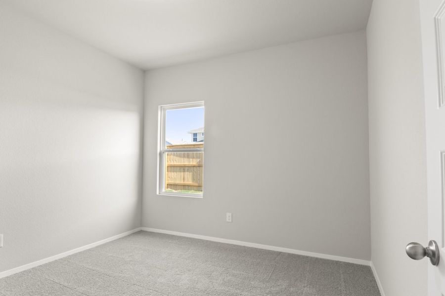 Image of a bedroom with tan carpeting and light grey walls with a window