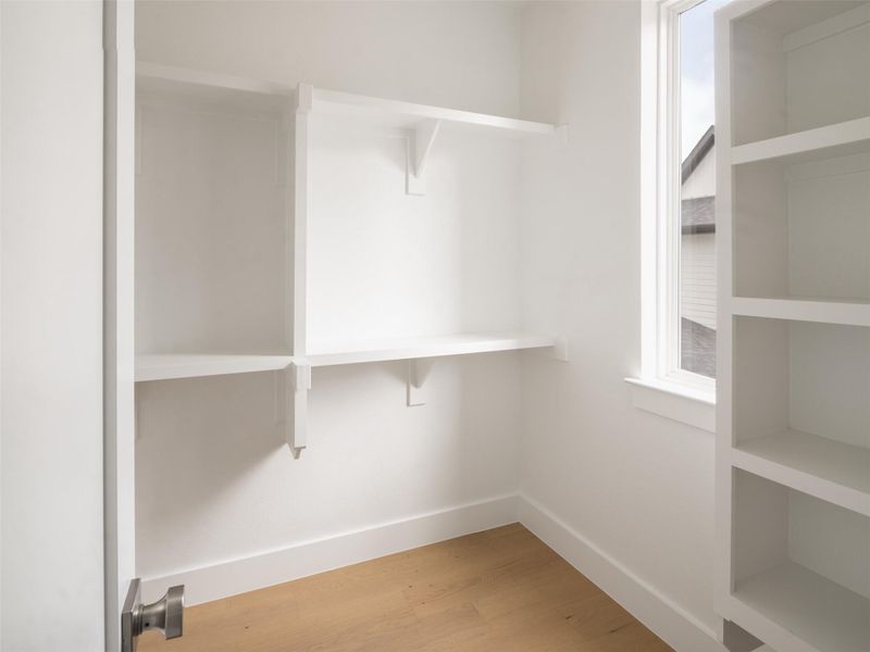Organized closet space featuring white built-in shelving, natural wood-finish flooring, and a bright window