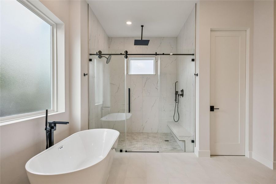 The freestanding soaking tub and glass-enclosed walk-in shower create a spa-inspired focal point within the primary bath. Oversized windows bring natural light into the space while maintaining privacy. The freestanding soaking tub and glass-enclosed walk-in shower create a spa-inspired focal point within the primary bath. Oversized windows bring natural light into the space while maintaining privacy.