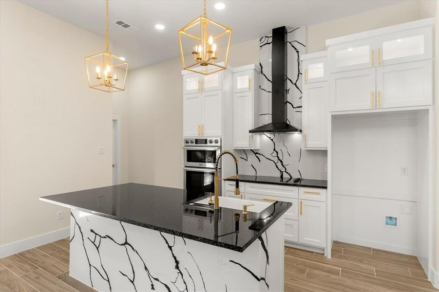 Kitchen with wood look tile floors, white cabinets, a kitchen island with sink, dark stone countertops, and double oven