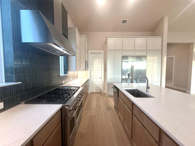 Kitchen with wall chimney exhaust hood, high end appliances, light wood-style flooring, backsplash, and light stone counters