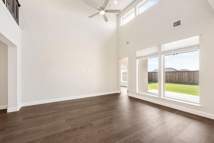 Open living room with two-story ceiling, dark hardwood floors, ceiling fan, and large windows overlooking backyard Open living room with two-story ceiling, dark hardwood floors, ceiling fan, and large windows overlooking backyard