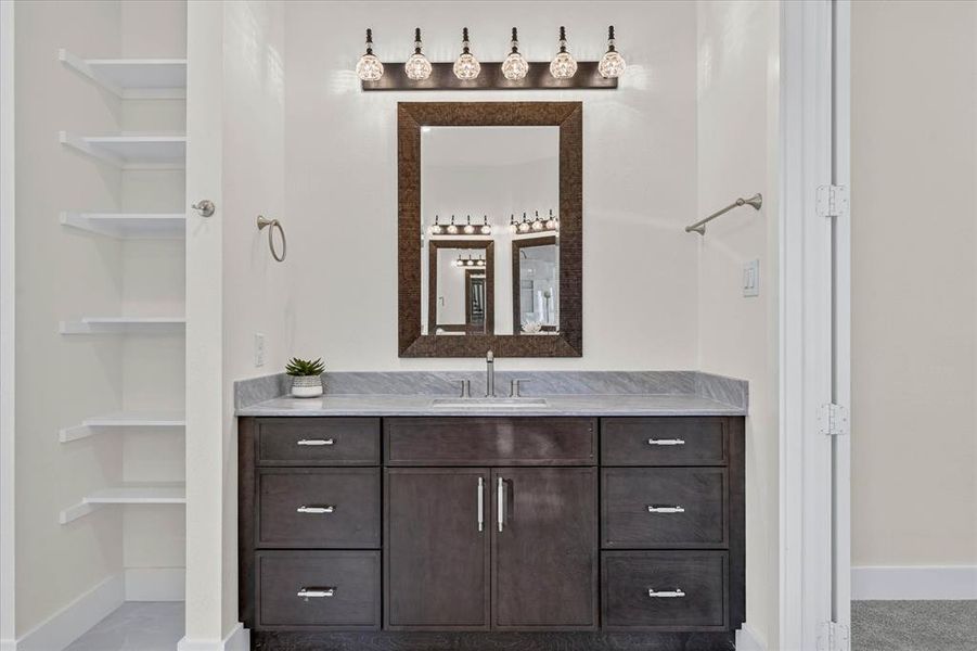 Bathroom vanity featuring a dark wood-finish cabinet with silver hardware, a light-toned countertop, and an undermount sink Bathroom vanity featuring a dark wood-finish cabinet with silver hardware, a light-toned countertop, and an undermount sink