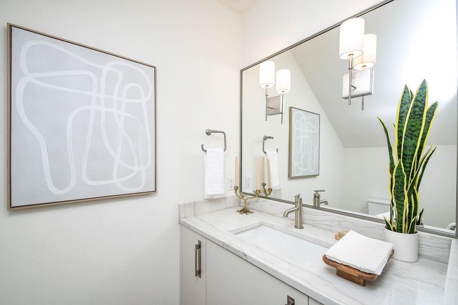 Modern bathroom with a sleek white vanity, marble countertop, and integrated sink. Features a large mirror, contemporary lighting, abstract wall art, and a potted plant for a touch of greenery.
