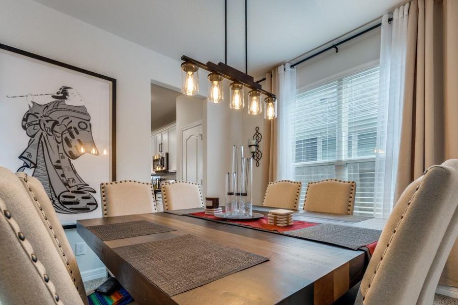 This dining room features a modern chandelier and a large window for natural light. The space is accented with elegant upholstered chairs and contemporary artwork, providing a cozy yet stylish atmosphere.