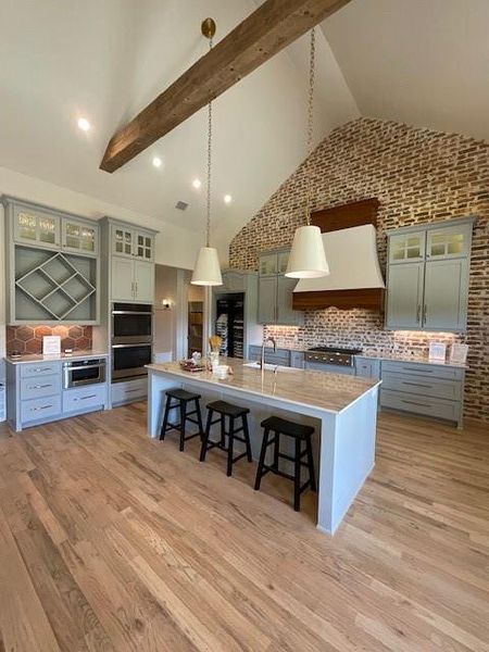 Kitchen with a center island with sink, hanging light fixtures, high vaulted ceiling, a breakfast bar area, and ventilation hood