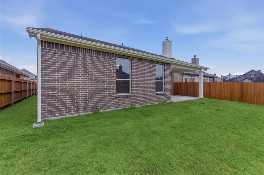 Spacious backyard featuring a covered patio, privacy fencing, and a brick exterior