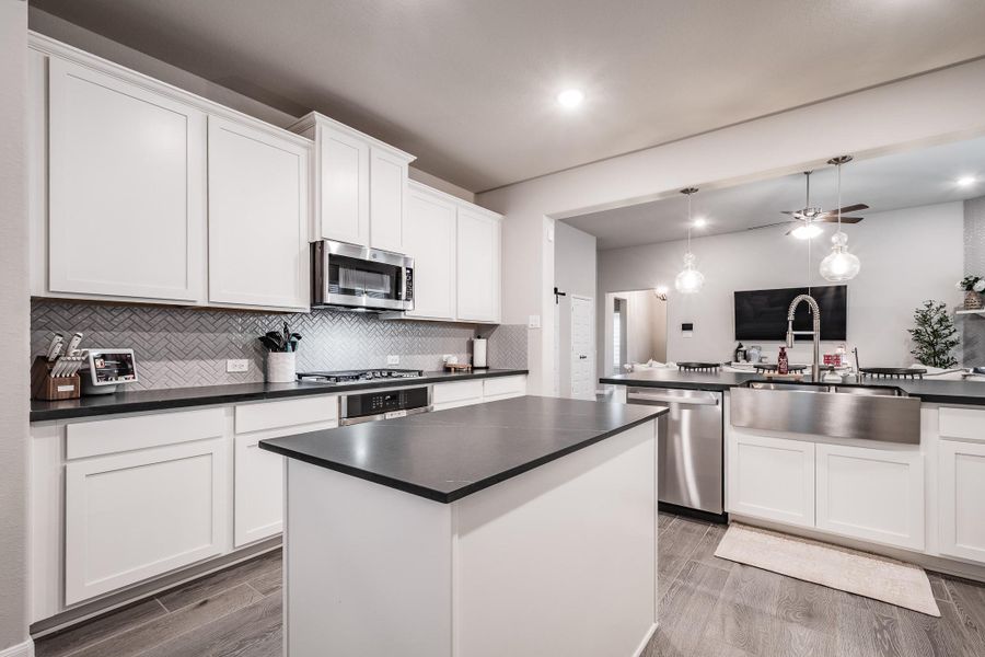 This photo showcases a modern kitchen with sleek white cabinetry and dark countertops. It features a large island, stainless steel appliances, and a stylish herringbone backsplash. The open layout includes pendant lighting and a farmhouse sink, creating a bright and inviting space. This photo showcases a modern kitchen with sleek white cabinetry and dark countertops. It features a large island, stainless steel appliances, and a stylish herringbone backsplash. The open layout includes pendant lighting and a farmhouse sink, creating a bright and inviting space.