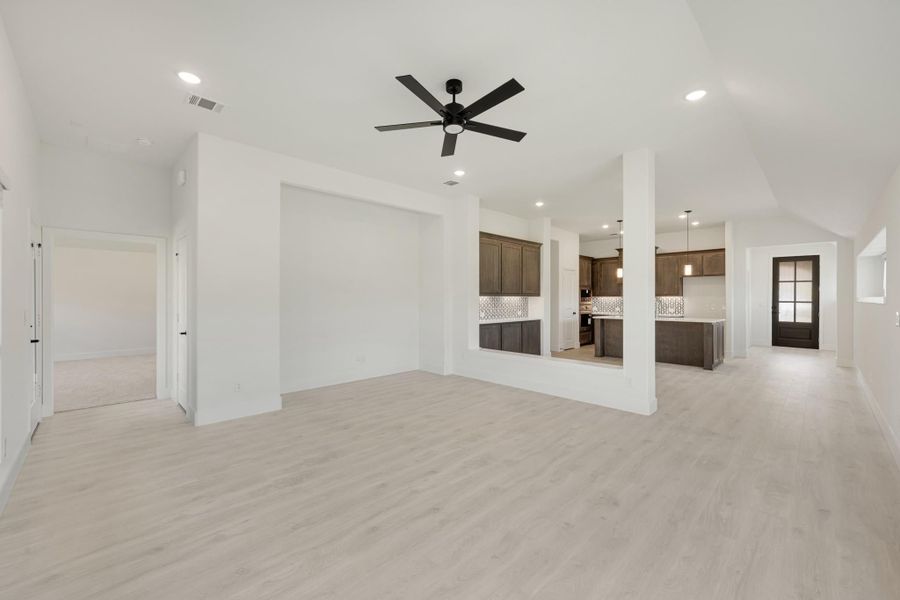 Open living area with light wood floors, ceiling fan, and open view to kitchen with dark cabinets