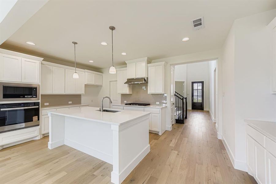 Kitchen featuring stainless steel appliances, decorative light fixtures, white cabinets, recessed lighting, and light wood-style flooring Kitchen featuring stainless steel appliances, decorative light fixtures, white cabinets, recessed lighting, and light wood-style flooring