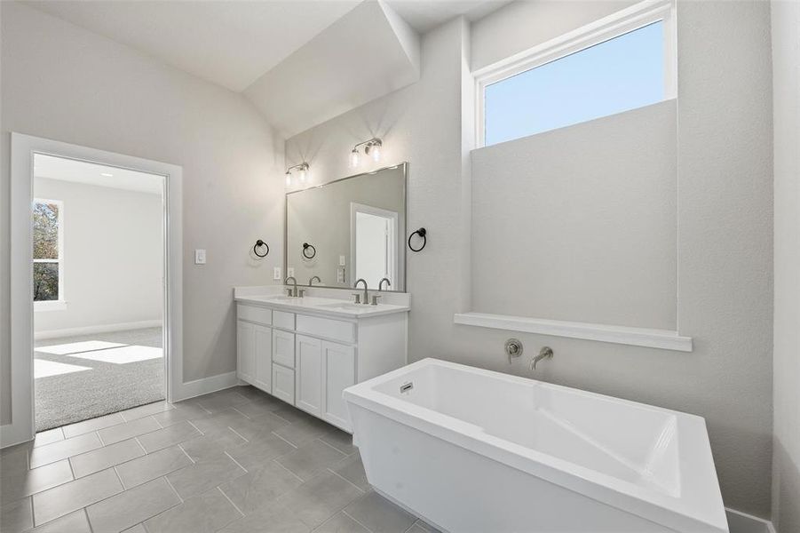 Bathroom featuring plenty of natural light, a freestanding bath, double vanity, vaulted ceiling, and light colored carpet Bathroom featuring plenty of natural light, a freestanding bath, double vanity, vaulted ceiling, and light colored carpet