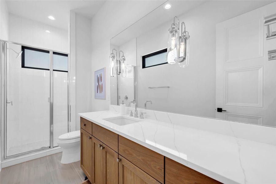 Bathroom four: Gleaming stone countertops and a spacious glass shower elevate this modern bathroom design.