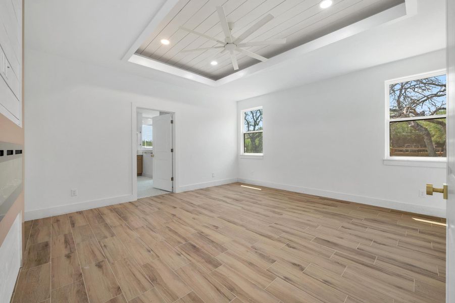 Bedroom with a tray ceiling, recessed lighting, light wood finished floors, and ensuite bath Bedroom with a tray ceiling, recessed lighting, light wood finished floors, and ensuite bath