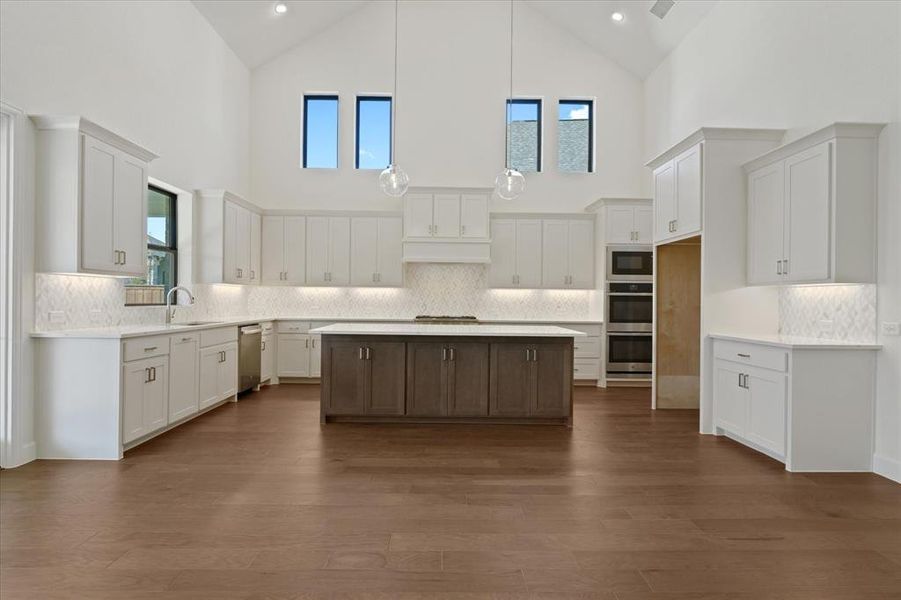 Kitchen featuring high vaulted ceiling, white cabinetry, decorative backsplash, a center island, and pendant lighting