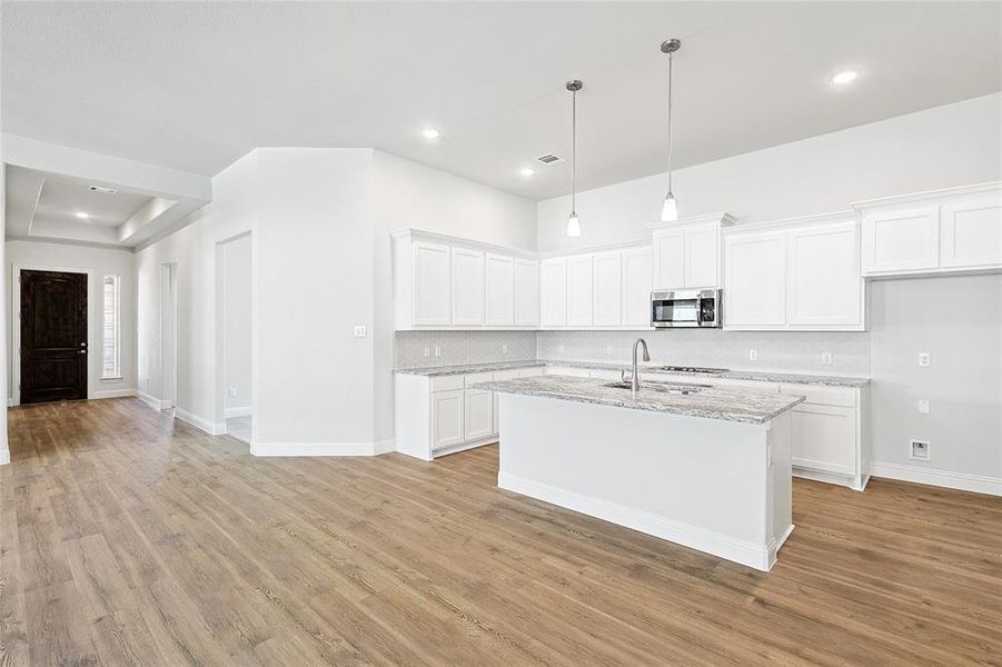 Kitchen featuring white cabinetry, pendant lighting, light stone countertops, a center island with sink, and light wood-style flooring
