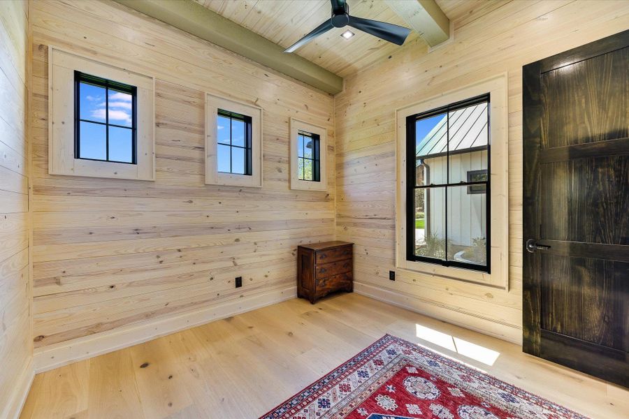 Empty room with light wood-style floors, ceiling fan, a wood ceiling with exposed beams, and wood walls