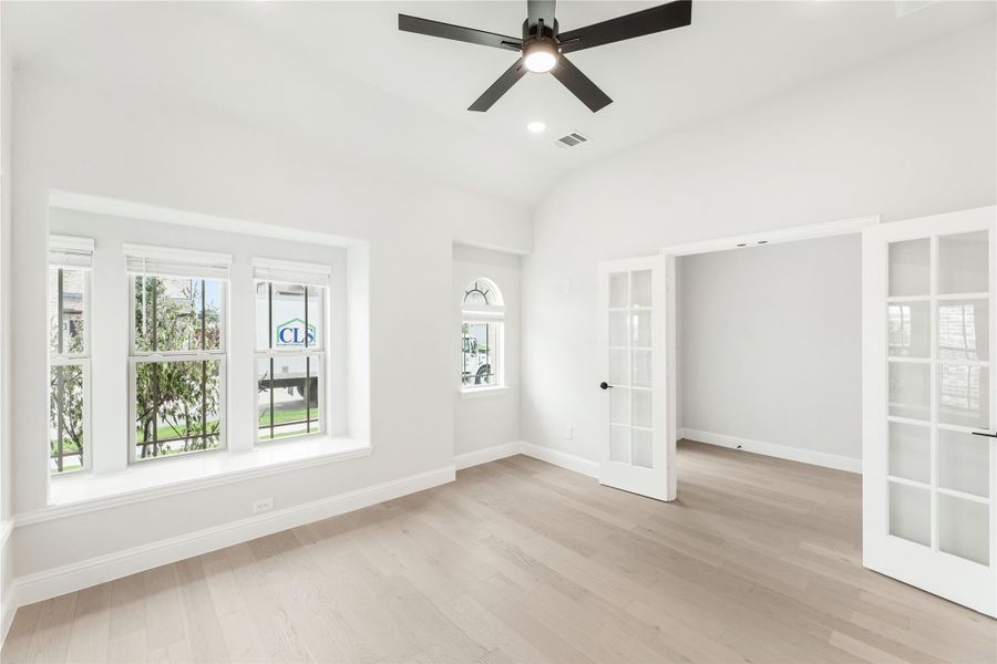 Empty room with vaulted ceiling, ceiling fan, light hardwood floors, and French doors