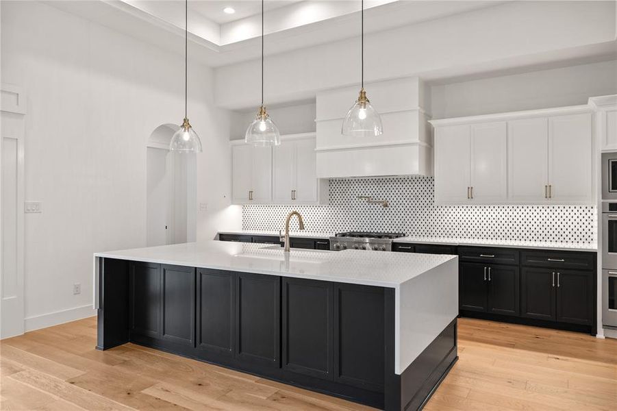 Kitchen featuring dark cabinets, tasteful backsplash, white cabinetry, and light wood finished floors Kitchen featuring dark cabinets, tasteful backsplash, white cabinetry, and light wood finished floors