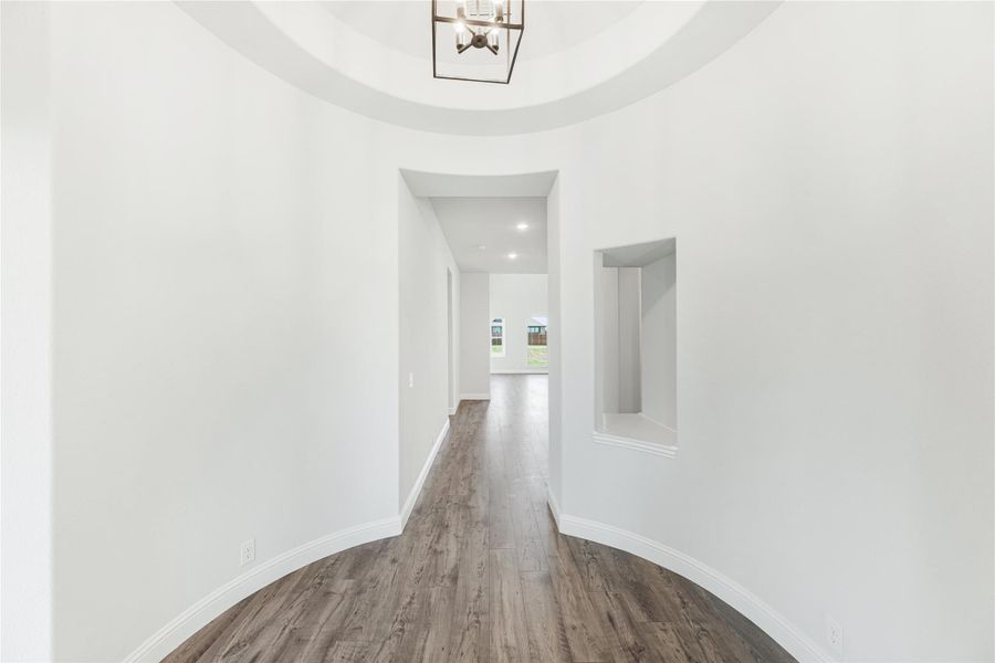 Entryway with round tray ceiling, pendant chandelier, hardwood floors, and hallway leading to main living area