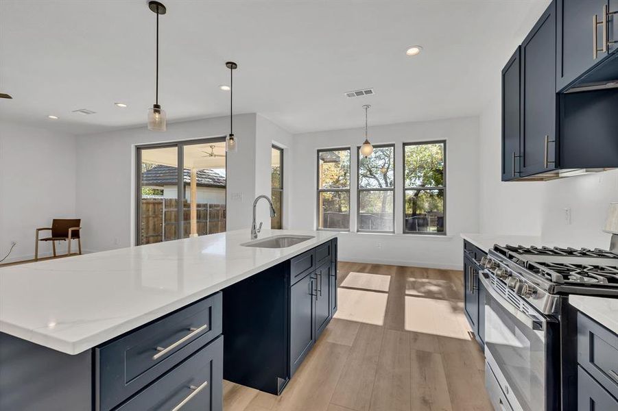 Kitchen with stainless steel gas stove, hanging light fixtures, light wood finished floors, light stone counters, and recessed lighting