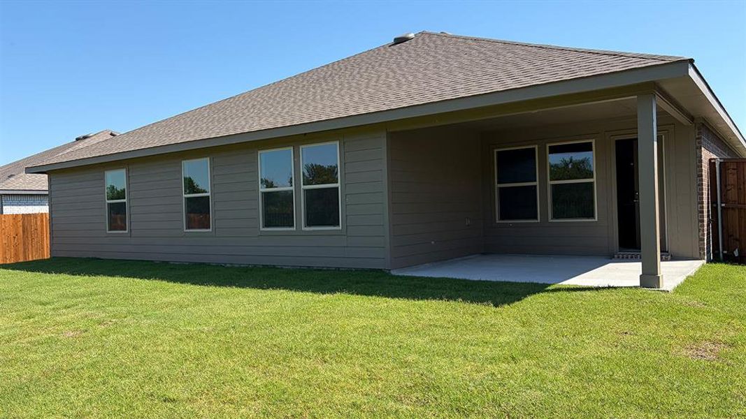 Rear exterior featuring a covered concrete patio, grey horizontal siding, numerous windows, a brown shingle roof, and a wood fence Rear exterior featuring a covered concrete patio, grey horizontal siding, numerous windows, a brown shingle roof, and a wood fence