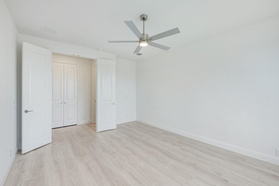 Empty bedroom with light wood floors, ceiling fan, and white double closet doors Empty bedroom with light wood floors, ceiling fan, and white double closet doors