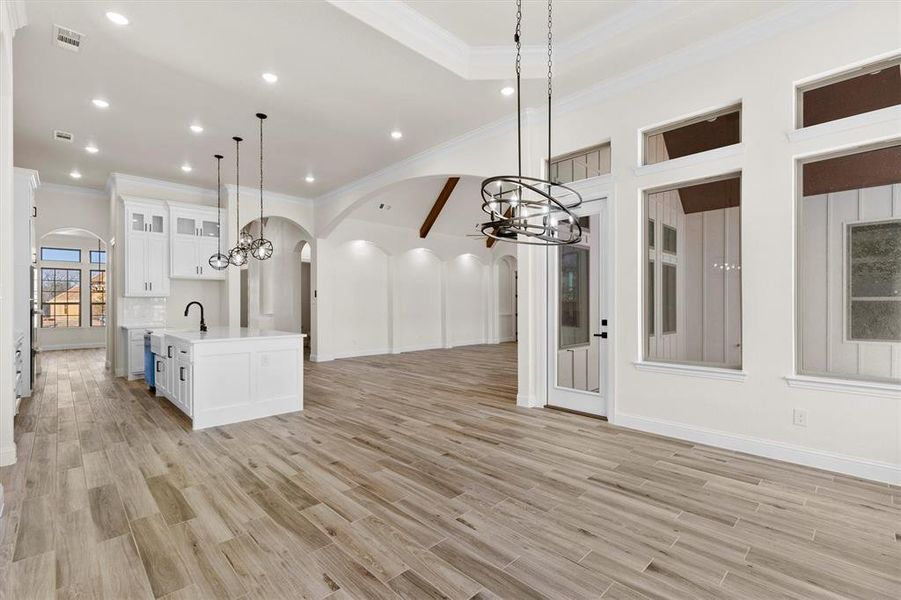 Kitchen featuring white cabinetry, pendant lighting, custom flooring, and an island with sink